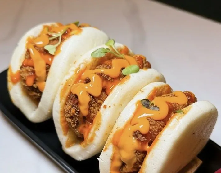 Butter chicken baos on a black tray.